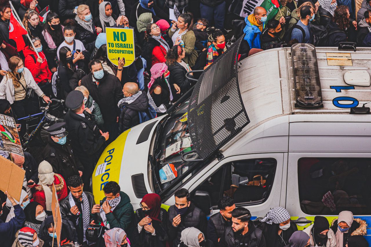 Crowd during protest against Israeli occupation with police vehicle in center.